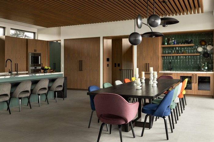 The dining room chairs – in six different colours – introduce a playful element to the space. The walnut slat ceiling, a feature that is repeated throughout the home, visually zones the open-concept space, improves acoustics and conceals custom, low-visibility track lighting placed along the slats.