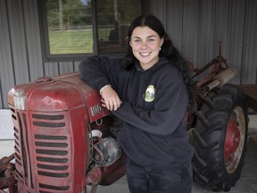 A young woman stands with an old tractor.