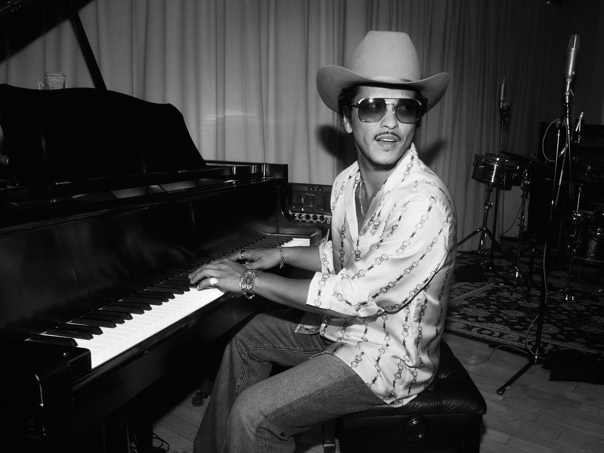 Black and white photo of Bruno Mars sitting at a piano.