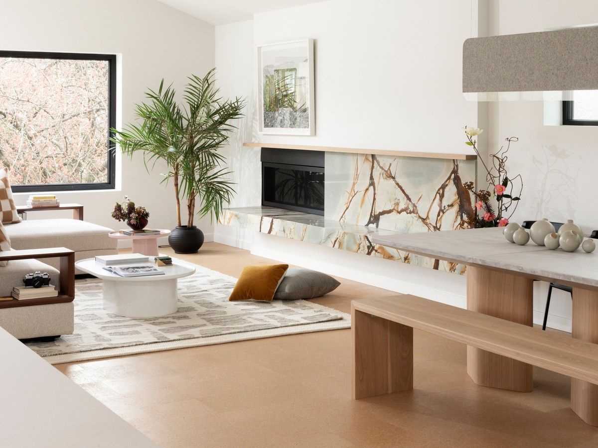 Blue Mare quartzite reappears in the living room, extending towards the dining room from a gas fireplace in a bench-like hearth. The fireplace remains in the original chimney-stack location, preserving the upstairs-downstairs hearth arrangement typical of a Vancouver Special.