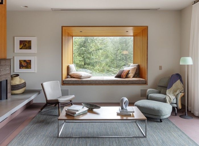 A fir-lined cantilevered bay window adds a reading nook to a compact living room, framing views into the forest.