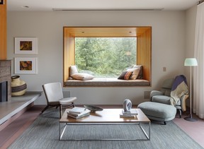 A fir-lined cantilevered bay window adds a reading nook to a compact living room, framing views into the forest.