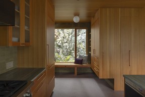 A compact mudroom pairs a built-in fir bench with full-height storage for coats and boots. Edge-grain Douglas fir continues in from exterior soffits, while green ceramic tile by Heath Ceramics, copper-plated hardware and a corner window overlooking a fern-planted rock face carry colours and materials from outside into the entry.