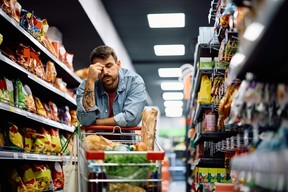 Mid adult man having a headache while buying groceries in supermarket.