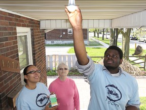 Peter Igboanugo (R) and Tonya Beal (L) of Enwin install an energy efficient light bulb on the porch of Hickory Road resident Idella Lazar in Windsor, Ont. on April 19, 2012. (Dan Janisse / The Windsor Star)