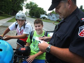 Senior Const. Mauro Tonin, right, gives out raffle tickets to Sacred Heart students, from left, Alex Cypcarz, 13, Anthony Mancini, 13, and Bryce Meillur, 13, (blue helmet), for following proper safety rules while riding their bikes in LaSalle, Friday, June 22, 2012. Tonin gave out the tickets as part of the Safety Cycling Program. (DAX MELMER/The Windsor Star)