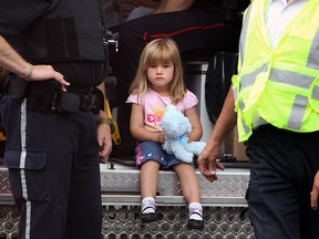 A young girl plays with a teddy bear as she sits at the back of an ambulance at the scene of fire in Windsor, Ont., on Thursday, July 19, 2012. Fire crews battled a blaze in the basement of a home in the 1100 block of Windermere Road. (The Windsor Star / TYLER BROWNBRIDGE)