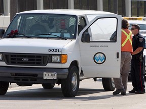 A police officer talks with a Windsor Utilities Commission employee at the corner of Memorial Drive and Howard Avenue in Windsor on July 6, 2012. A 48-year-old man was found slumped over the wheel of a van and later taken to hospital. (The Windsor Star / TYLER BROWNBRIDGE)