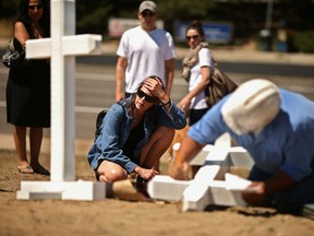 A woman prays as Greg Zanis of Aurora, Illinois, writes the names on the twelve crosses he made for a makeshift memorial to the victims of last July's mass shooting at the Century 16 movie theater in Aurora, Colorado. A carpenter by trade, Zanis made 26 crosses for the victims of the Newtown massacre as well. (Photo by Chip Somodevilla/Getty Images)