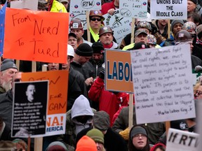 Demonstrators carry signs during a protest outside the Capitol building in Lansing, Michigan, U.S., on Tuesday, Dec. 11, 2012. Chanting labor supporters flooded the Capitol to protest Republican efforts to prohibit mandatory union dues in the home state of the United Auto Workers Union and the three largest U.S. automakers. Photographer: Jeff Kowalsky/Bloomberg
