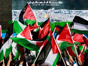In this file photo, Palestinians wave Palestinian flags as they walk past a banner showing the Dome of the Rock Mosque in the Al Aqsa Mosque compound in Jerusalem's old city, during celebrations for their successful bid to win U.N. statehood recognition in the West Bank city of Ramallah, Sunday, Dec. 2, 2012. Israel has rejected the borders of a future Palestinian state the U.N. endorsed last week and on Friday, Israel announced it would press ahead plans to build thousands of settler homes. And it is punishing the Palestinians further by withholding more than $100 million in taxes and other funds collected on their behalf. (AP Photo/Nasser Shiyoukhi)