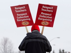 A teacher with the Ottawa-Carleton District School Board carries picket signs at Roberta Bondar Public School in protest to Ontario's Bill 115, Wednesday, Dec. 12, 2012 in Ottawa. THE CANADIAN PRESS/Cole Burston