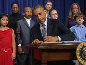 U.S. President Barack Obama signs a series of executive orders about the administration's new gun law proposals as children who wrote letters to the White House about gun violence, (L-R) Hinna Zeejah, Taejah Goode, Julia Stokes and Grant Fritz, look on in the Eisenhower Executive Office building January 16, 2013 in Washington, DC. One month after a massacre that left 20 school children and 6 adults dead in Newtown, Connecticut, the president unveiled a package of gun control proposals that include universal background checks and bans on assault weapons and high-capacity magazines. (Photo by Chip Somodevilla/Getty Images)