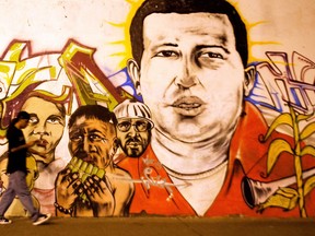 A man walks before a mural bearing the portait of Venezuelan President Hugo Chavez on March 5, 2013 in Cali, department of Valle del Cauca, Colombia. Chavez lost his battle with cancer, silencing the leading voice of the Latin American left and plunging his divided oil-rich nation into an uncertain future. AFP PHOTO / LUIS ROBAY