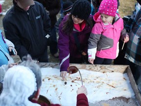 In this file photo, Nancy Hager, bottom, pours hot syrup over cold snow to produce taffy for families to taste at the Maple Syrup Festival at the John R. Park Homestead Conservation Area in Essex, Ont., Sunday, March 3, 2013.    (DAX MELMER/The Windsor Star)