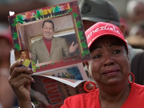 A woman holds a picture of President Hugo Chavez outside the military hospital where he died Tuesday in Caracas, Venezuela, Wednesday, March 6, 2013. Seven days of mourning were declared, all school was suspended for the week and friendly heads of state were expected for an elaborate funeral Friday..(AP Photo/Ariana Cubillos)