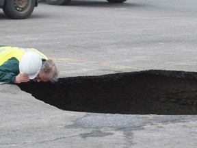 A man looks inside a sinkhole that opened up at a parking lot at Montreal Airport on Friday, March 29, 2013, after two partially-submerged cars were pulled from the hole. (Graham Hughes / The Canadian Press)