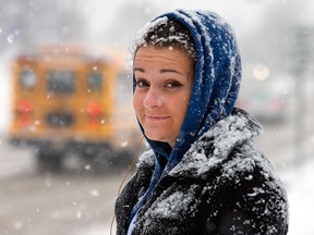 Rachel Bergsma can only grin and bear it while waiting for a bus on Clyde Ave that was at least a half hour late as the region is hit with a late winter snowfall. (Wayne Cuddington / Ottawa Citizen)