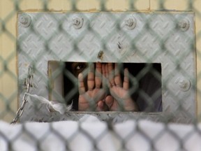 In this Dec. 4, 2006 file photo reviewed by a U.S. Dept of Defense official, a detainee shields his face as he peers out through the so-called "bean hole" which is used to pass food and other items into detainee cells, at Camp Delta detention centre, Guantanamo Bay U.S. Naval Base, Cuba. Lt. Col. Samuel House said Saturday, April 27, 2013 that 100 men are now on strike, up six from Thursday. The hunger strike began in February 2013, with prisoners protesting conditions and their indefinite confinement. The U.S. holds 166 prisoners at Guantanamo, most without charges. (AP Photo/Brennan Llinsley)