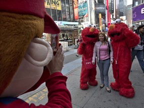 A Super Mario character, left, uses a woman's mobile phone camera to photographer her with a pair of Elmo characters in New York's Times Square, Tuesday, April 9, 2013. A string of arrests in the last few months has brought unwelcome attention to the growing number of people, mostly poor immigrants, who make a living by donning character outfits, roaming Times Square and charging tourists a few dollars to pose with them in photos. (AP Photo/Richard Drew)