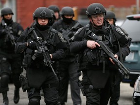 Police in tactical gear conduct a search for a suspect in the Boston Marathon bombings, Friday, April 19, 2013, in Watertown, Mass. The bombs that blew up seconds apart near the finish line of the Boston Marathon left the streets spattered with blood and glass, and gaping questions of who chose to attack and why. (AP Photo/Matt Rourke)