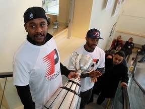 Walter Spencer, left, of the Toronto Argonauts is followed by the Montreal Alouettes' Daryl Townsend as he carries the Grey Cup up the escalator at Windsor Regional Hospital. (TYLER BROWNBRIDGE / The Windsor Star)