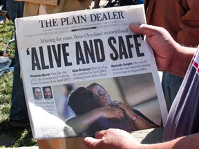 A man shows page one of The Plain Dealer newspaper to a friend while people gather along Seymour Avenue near the house where three women, who disappeared as teens about a decade ago, were found alive, May 7, 2013 in Cleveland, Ohio. Amanda Berry, who went missing in 2003, Gina DeJesus, who went missing in 2004, and Michelle Knight, who went missing in 2002, managed to escape their captors on May 6, 2013. Three suspects, all brothers, were taken into custody.   (Photo by Bill Pugliano/Getty Images)