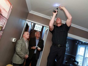 Rotary Club president Chris Woodrow, left, and Councillor Percy Hatfield watch as firefighter Lindsay Tod installs a smoke detector in a home in Windsor on Tuesday, May 14, 2013. Volunteers will go door-to-door installing smoke detectors under a new program. (TYLER BROWNBRIDGE/The Windsor Star)