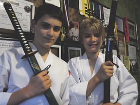 Evan Kozolanka (left) and his older brother Zack (right) pose with samurai swords in their Tecumseh home Sunday, June 2 in front of a wall displaying many awards and medals they have won in the South Korean martial art of hapkido. (Photo by/Rob Benneian)