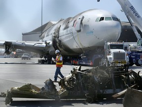 In a photograph taken through a fence, a man walks past wreckage of Asiana Flight 214, which crashed on Saturday, July 6, 2013, at San Francisco International Airport, at a news conference in San Francisco, Friday, July 12, 2013. A San Francisco Bay Area TV station has apologized after reporting bogus names of the four pilots aboard Asiana Airlines flight 214 that were a play on Asian names. (/Jeff Chiu/Associated Press)