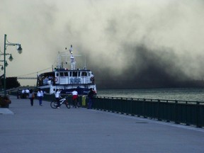 Bystanders along Windsor's riverfront watch as a cloud of petcoke appears to drift across the Detroit River. (Twitpic/The Windsor Star)