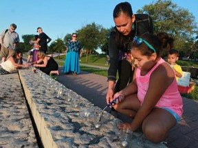 Windsor First Nations supporters Michelle Nahdee helps 9-year-old Kiara Mitchell light a candle at the Honour the Apology vigil on Windsor's riverfront on July 25, 2013. (Dax Melmer / The Windsor Star)