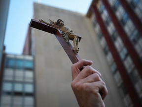 Michael Cowan holds a crucifix in the air as he joins approximately 50 people protesting the removal of a large steel cross from Hotel-Dieu Grace Hospital on Ouellette Ave., Friday, Sept. 27, 2013. (DAX MELMER/The Windsor Star)