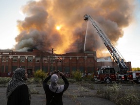 Women take photos as Detroit Firefighters battle a commercial building fire on Thursday, Sept. 26, 2013, in Detroit. The large, vacant building once housed a trucking company and a bread factory. No injuries were reported. (AP Photo/Detroit Free Press, Ryan Garza)