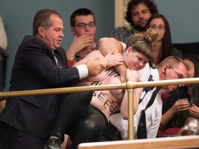 A topless Femen activist is carried out of the legislature visitor section by security after protesting the presence of the crucifix inside the legislature in Quebec City on Tuesday, October 1, 2013. (THE CANADIAN PRESS/Jacques Boissinot)