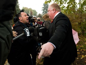City of Toronto Mayor Rob Ford, right, pushes members of the media off his property as he leaves his home in Toronto on Thursday, Oct. 31, 2013. THE CANADIAN PRESS/Nathan Denette