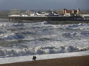 People walks along the shoreline as waves crash onto the beach in Brighton, England, Monday, Oct. 28, 2013. A major storm with hurricane force winds is lashing much of Britain, causing flooding and travel delays with the cancellation of many flights and trains. Weather forecasters say it is one of the worst storms to hit Britain in years. (AP Photo/Sang Tan)