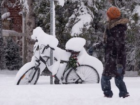 A woman walks past a bicycle covered in snow, Wednesday November 27, 2013 in Ottawa. An overnight storm dropped 20 centimetres on the region with ten centimetres more expected throughout the day. THE CANADIAN PRESS/Adrian Wyld