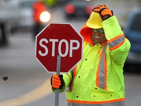 Sign man Guy Jehu hangs onto his hard hat, Mon. Nov. 18, 2013, as a gust of wind kicked up. The Coco Paving employee was part of a crew doing road repairs on Riverside Dr. E. near Riverdale Ave.    (DAN JANISSE/The Windsor Star)