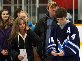 Kathy Hyland, left, wipes a tear after her son Spencer Hyland, right, and husband Chris Hyland, behind,  received an envelope from E. J. Lajeunesse and Tecumseh Vista Academy fundraising hockey game at Tecumseh Arena.  Hundreds of students and faculty attended the game which raised thousands for the family, Monday December 2, 2013.  (NICK BRANCACCIO/The Windsor Star)