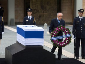 Israel's President Shimon Peres lays a wreath next to the coffin of late Israeli Prime Minister Ariel Sharon at the Knesset plaza, Israel's Parliament, in Jerusalem, Sunday, Jan. 12, 2014. Sharon, the hard-charging Israeli general and prime minister who was admired and hated for his battlefield exploits and ambitions to reshape the Middle East, died Saturday, eight years after a stroke left him in a coma from which he never awoke. He was 85.  Hebrew on wreath reads: "The State of Israel." (AP Photo/Sebastian Scheiner)
