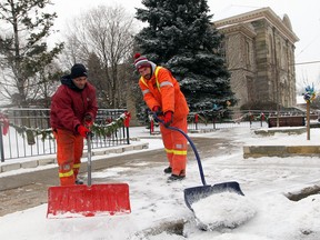 City of Windsor workers Rob Kolodie, left, and Mike Trepanier shovel snow from the sidewalks around Mackenzie Hall in Olde Sandwich Towne to get a head start on the snowfall Wednesday, January 1, 2014. Environment Canada says the area could see up to 21 cm of snow by the end of Thursday. (NICK BRANCACCIO/The Windsor Star)