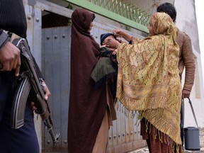 In this file photo, a Pakistani policeman stands guard as a health worker administers polio vaccine drops to a child during a door-to-door polio immunization campaign on the outskirts of Islamabad on January 22, 2014.  At least seven people were killed in a bomb attack on a police van taking officers to guard polio vaccination teams in restive northwest Pakistan, officials said.  Militant attacks and threats of violence have badly affected efforts to stamp out the crippling disease in Pakistan, one of only three countries where it remains endemic. (Aamir Qureshiaamir Qureshi/AFP/Getty Images)