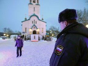 A policeman watches a believer leaving the Cathedral of the Resurrection of Christ in Yuzhno-Sakhalinsk on Sunday, Feb. 9, 2014. Law enforcement officers detained a man, who worked as a security guard, and were trying to determine why he attacked the Russian Orthodox cathedral in the city of Yuzhno-Sakhalinsk, the federal Investigative Committee said in a statement. A gunman opened fire Sunday in a cathedral on Russia's Sakhalin Island in the Pacific, killing a nun and a parishioner and wounding six others, investigators said. Concerns about security in Russia are especially high because of the Winter Olympics in Sochi, but there was no apparent connection to the games. Sakhalin Island is about 7,500 kilometers (more than 4,500 miles) from Sochi. (AP Photo/ Dmitriy Sindyakov)