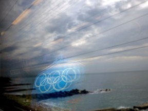 The Olympic rings on the back of a jacket of a worker are reflected in a train window as it travels from the Olympic Park to the Sochi city centre along the Black Sea, Monday, Feb. 10, 2014, in Sochi, Russia, home to the 2014 Winter Olympics. (AP Photo/David Goldman)