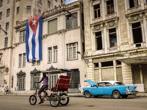 A bike-taxi and a vintage American car are seen in front of a building decorated with a large Cuban flag, on December 31, 2013, in Havana. (Adalberto Roque/AFP/Getty Images)