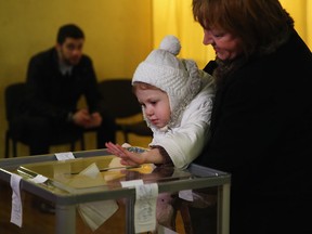 In this file photo, a woman holds a young child up to post a ballot paper for her inside a polling station in Simferopol on March 16, 2014 in Simferopol, Ukraine. (Photo by Dan Kitwood/Getty Images)