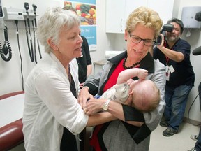 In this file photo, Premier Kathleen Wynne takes baby Lucas from his grandmother Cathy Caissie to help weigh him at a family health care unit on a campaign stop in Lindsay, Ont. on Friday, May 30, 2014. THE (CANADIAN PRESS/Fred Thornhill)
