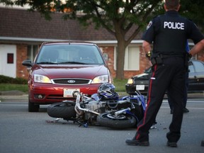 A Windsor police officer stands over the scene of a crash between a motorcycle and Ford Focus at Dougall Avenue and Eugenie Street on Friday, July 4, 2014. The motorcyclist was taken to hospital with unknown injuries. (DAX MELMER/The Windsor Star)