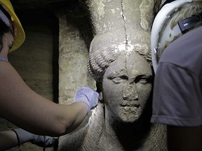In this photo released on Sunday, Sept. 7, 2014 by the Greek Culture Ministry, archaeologists inspect a 60cm (2 foot) female figurine on a wall leading to the yet unexplored main room of an ancient tomb, in the town of Amphipolis, northern Greece. The tomb dates between 325 B.C. â€” two years before the death of ancient Greek warrior-king Alexander the Great â€” and 300 B.C. Archaeologists excavating a massive burial mound in northern Greece have found two marble sculptures of female figures and a large, colored marble panel in what appears to be the antechamber of the main room. (AP Photo/Culture Ministry)